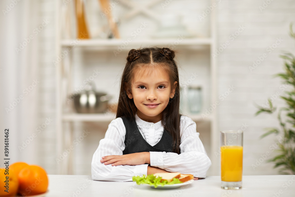 happy little child girl in school uniform having breakfast - sandwich and orange juice in the kitchen. healthy breakfast happy little child girl in school uniform having breakfast - sandwich and orange juice in the kitchen. healthy breakfast
