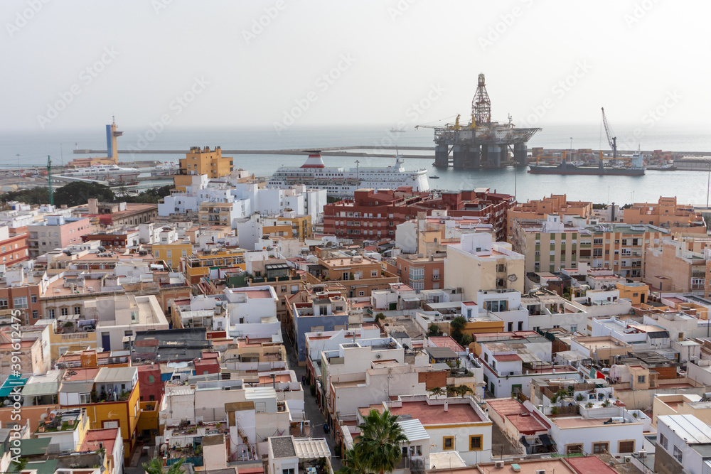 Urban harbor with oil platform and cruise boats anchored, Mediterranean city with white houses and flat roofs, mobile cranes at the port Almería, Andalusia, South of Spain