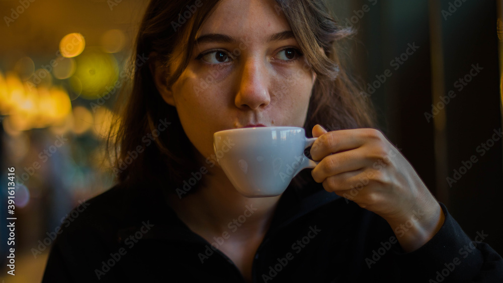 A young woman drinking a cup of coffee from porcelain in a cafe. Blurry background. A young woman drinking a cup of coffee from porcelain in a cafe. Blurry background.
