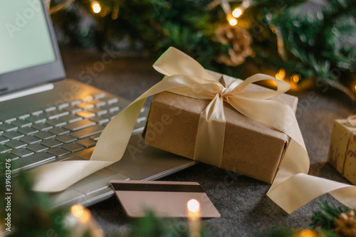 Christmas shopping online with a credit card for the holiday. Laptop with gifts on the table next to fir branches and a garland of lights