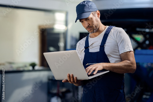 Mid adult repairman using laptop at car workshop. photo
