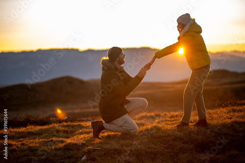 Silhouettes of a man making a marriage proposal to his girlfriend on the mountain peak at sunset. Landscape with the silhouette of lovers against the colorful sky. photo