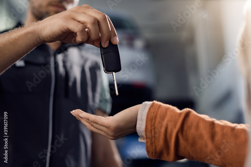 Close-up of woman receiving car key from auto mechanic in a workshop.