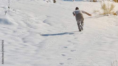 young boy running playing in the snow on a sunny day, happy with the cold