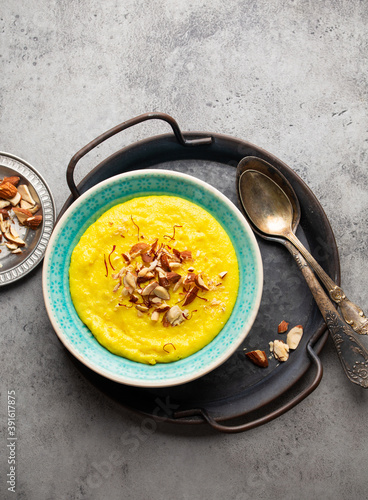 Traditional Indian dish Kheer, sweet rice milk pudding with almonds and saffron in blue ceramic bowl with spoons on stone rustic background, top view. Dessert meal of Indian cuisine