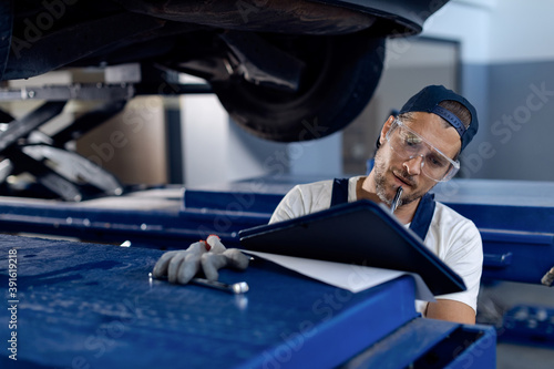 Auto repairman taking notes while examining a vehicle in a workshop.