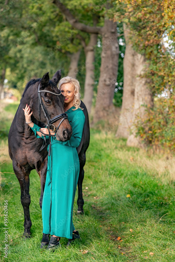Happy beautiful blond girl taking care of her horse outdoors. Selective focus on the horse, narrow depth of field, direct sunlight, copy-space Happy beautiful blond girl taking care of her horse outdoors. Selective focus on the horse, narrow depth of field, direct sunlight, copy-space