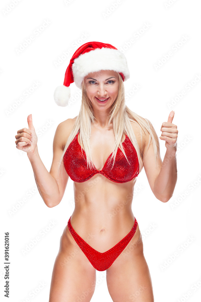 Bodybuilder blonde woman wearing a red bathing suit, wearing a Santa hat, is standing showing thumbs up isolated on white background Bodybuilder blonde woman wearing a red bathing suit, wearing a Santa hat, is standing showing thumbs up isolated on white background