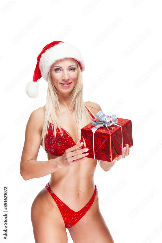 Bodybuilder blonde woman wearing a red bathing suit, wearing a Santa hat, is standing holding a present isolated on white background Bodybuilder blonde woman wearing a red bathing suit, wearing a Santa hat, is standing holding a present isolated on white background