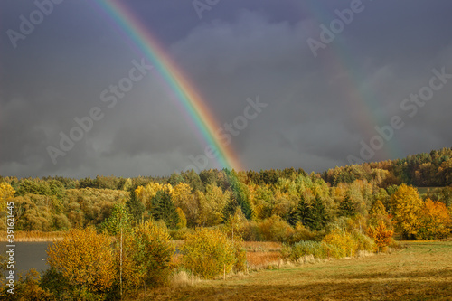 Double rainbow in countryside. Beautiful intense rainbow colors in rainy day.Weather forecast.Fall rural landscape with rainbow over dark dramatic stormy sky.Freedom happiness concept.