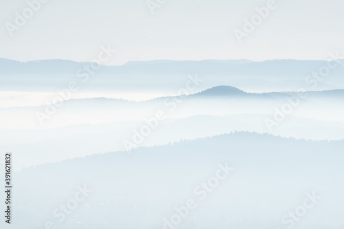 mystical and romantic bright scenery with layers of mountaintops softly peaking out of white clouds. Beautiful landscape with soft hills in a winter atmosphere lit by the setting sun