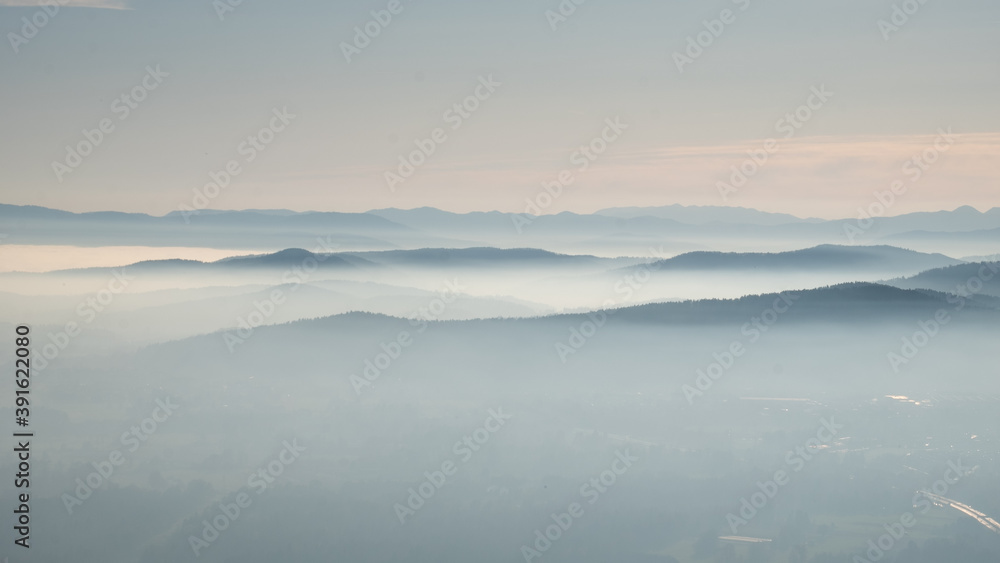 mystical and romantic bright scenery with layers of mountaintops softly peaking out of white clouds. Beautiful landscape with soft hills in a winter atmosphere lit by the setting sun