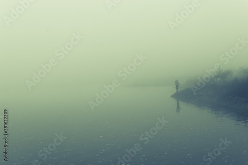 Fog on the river and silhouette of a fisherman with a rod on the river bank.