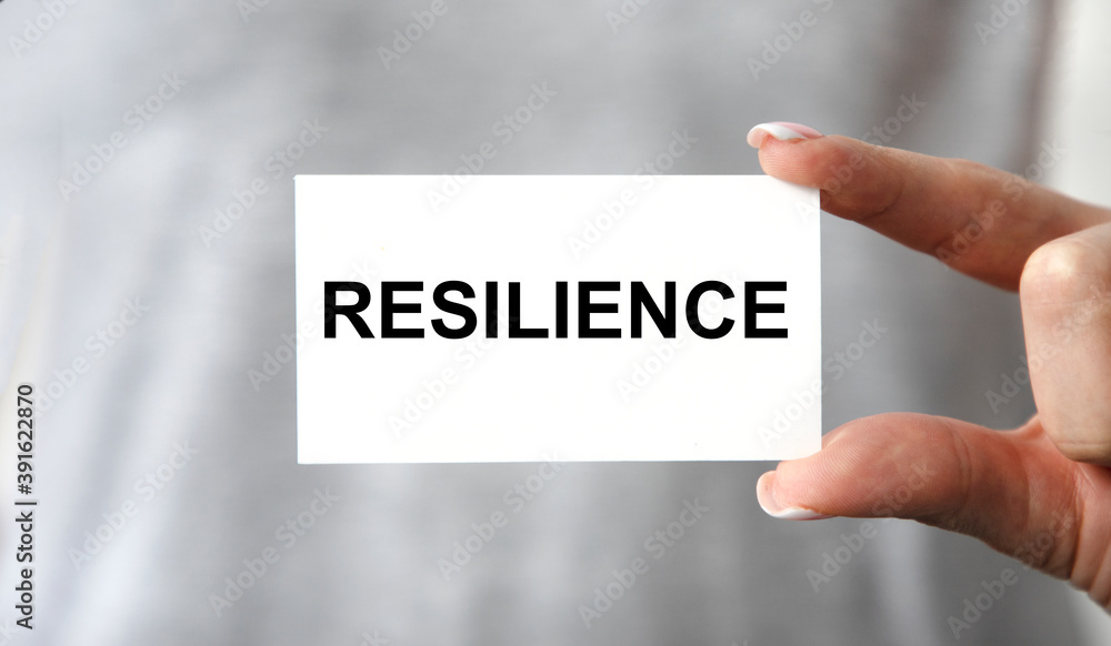 The girl holds in front of her a card with the text OF RESILIENCE, next to a pen, graphics. The girl holds in front of her a card with the text OF RESILIENCE, next to a pen, graphics.