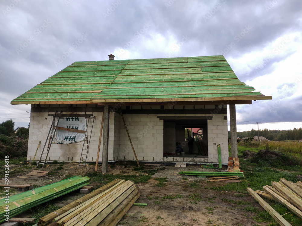 Front view on house under construction. House In basic state. Detached house under construction in small village. Located on fenced plot. Lack of roof covering, roof windows. Front view on house under construction. House In basic state. Detached house under construction in small village. Located on fenced plot. Lack of roof covering, roof windows.