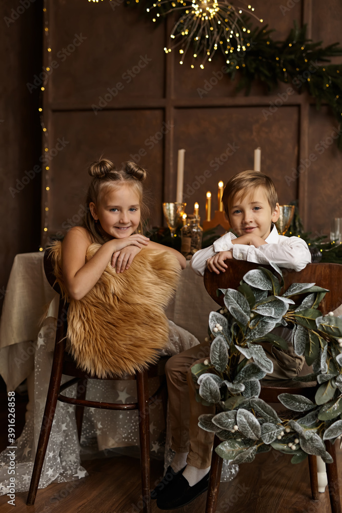Two children sit on chairs near a festive table