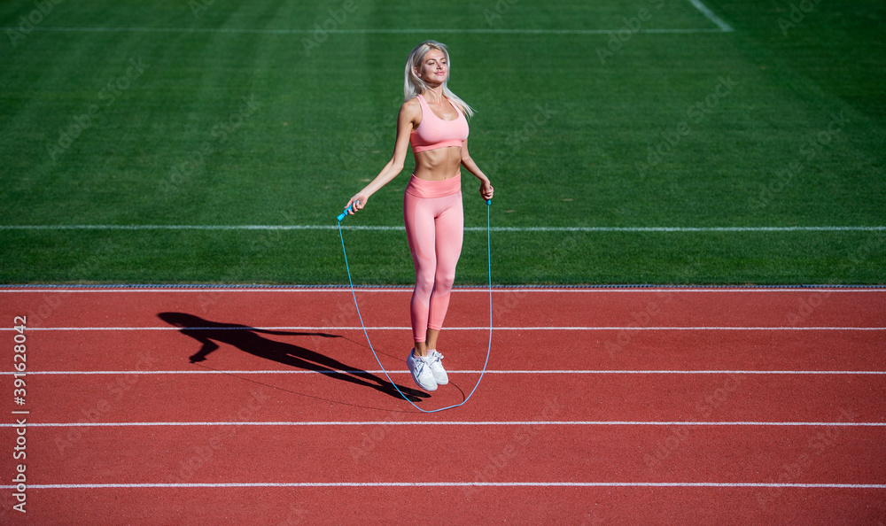 Obraz premium sexy lady in fitness sportswear. jumping on outdoor arena. training and workout. athletic female coach with skipping rope. woman sport trainer. healthy sporty lifestyle. health and energy