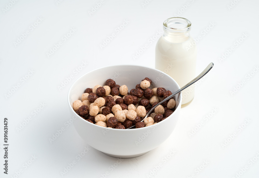 Cereal and chocolate balls in a white bowl and milk in a bottle on a light background. Side view. The concept of healthy, dietary breakfasts. Cereal and chocolate balls in a white bowl and milk in a bottle on a light background. Side view. The concept of healthy, dietary breakfasts.