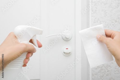 Young adult woman hands holding paper napkin and spray bottle. Disinfection white door handle. Closeup. General or regular cleanup. Point of view shot. 