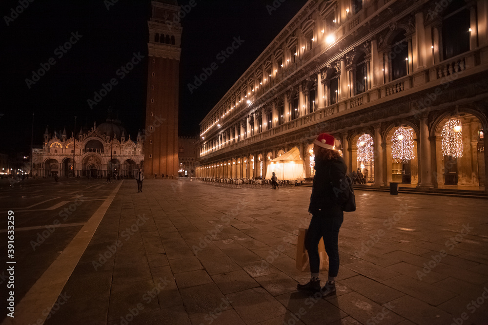 Woman with Christmas hat and shopping bag while looking at St. Mark's Square at night, Venice, Italy