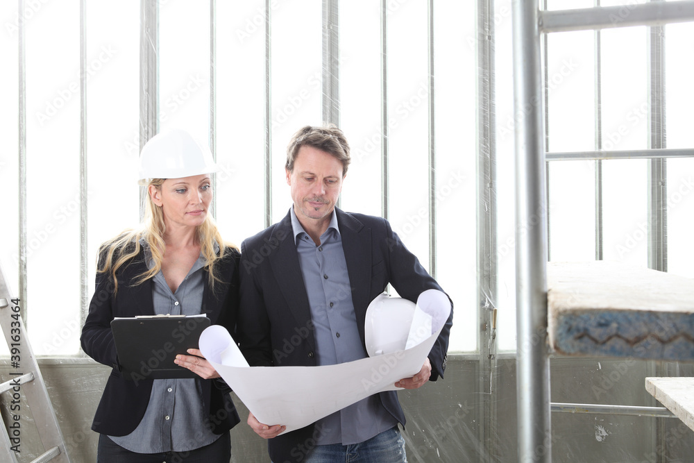 Fototapeta premium man and woman architects or engineers work together discussing with blueprint in the inside the construction building site