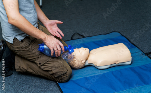 Man using CPR technique on dummy in first aid class. Oxigen mask on medical doll.