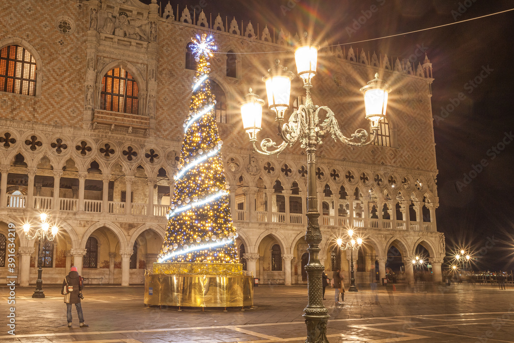 Night view of Christmas tree in front of Palazzo Ducale, San Marco square, Venice, Italy. Trail effect of unrecognizable people in motion
