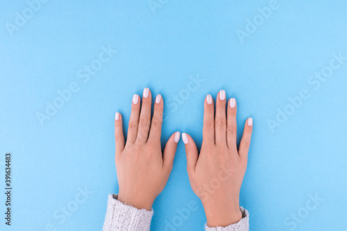 Stylish trendy female manicure. Beautiful nude nails on blue background. Nail polish. Art manicure. Modern style.