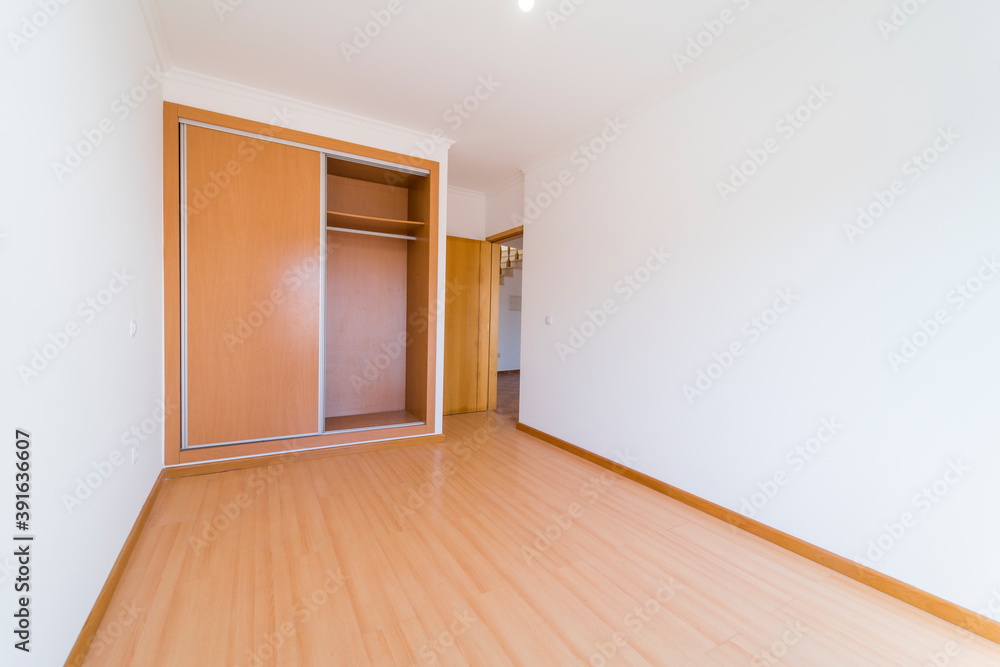 Empty room with dark wooden floating laminate flooring and wardrobe. House interior, wide bedroom space. Newly recently painted new apartment or house. Wood floor. Real state and property management Empty room with dark wooden floating laminate flooring and wardrobe. House interior, wide bedroom space. Newly recently painted new apartment or house. Wood floor. Real state and property management