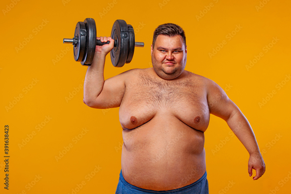 Fat man doing workout traning with dumbbells. Happy guy isolated over yellow background. Fat man doing workout traning with dumbbells. Happy guy isolated over yellow background.