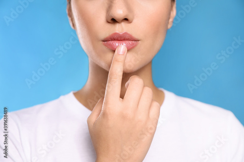 Woman with herpes touching lips on light blue background, closeup photo