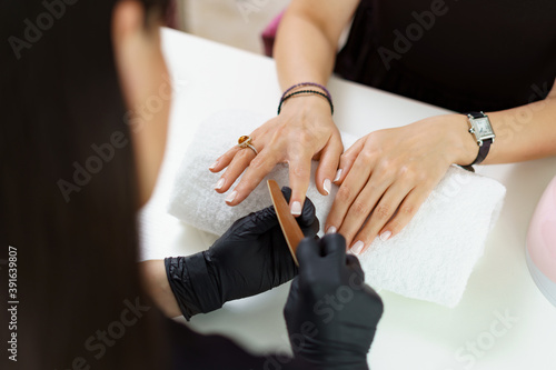 Close up details of woman hands in black gloves making manicure in luxury beauty salon with modern equipment  soft colors  nail service  perfect client hands.