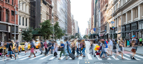 Busy street scene in New York City with groups of people walking across a crowded intersection on Fifth Avenue in Midtown Manhattan