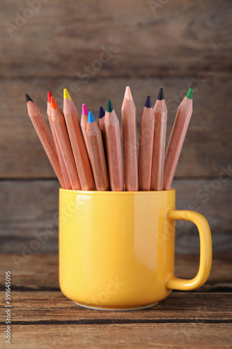 Colorful pencils in cup on wooden table