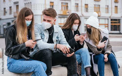 Group of young friends wearing face masks, using their smart phones and wearing winter clothes