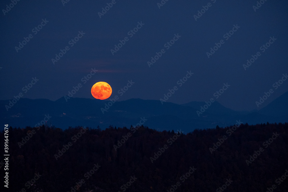 huge orange full moon rising behind a mountain ridge with layers of hills in the foreground creating a mystical atmosphere. glowing super moon rising into the night sky huge orange full moon rising behind a mountain ridge with layers of hills in the foreground creating a mystical atmosphere. glowing super moon rising into the night sky