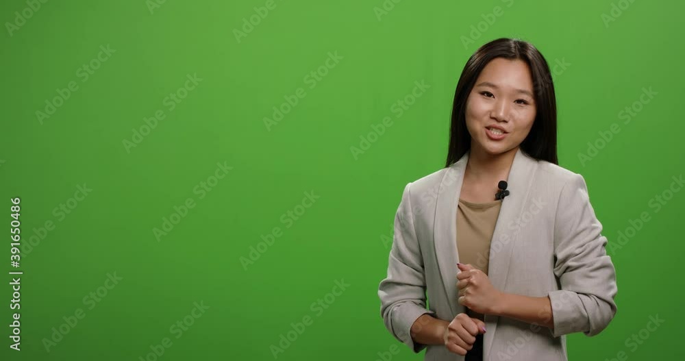 Positive asian woman looking at camera and talking during an advertisement. Female anchor during morning news report, shot on green background 4k footage Positive asian woman looking at camera and talking during an advertisement. Female anchor during morning news report, shot on green background 4k footage