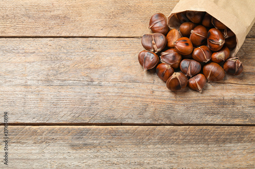 Delicious roasted edible chestnuts in paper bag on wooden table. Space for text