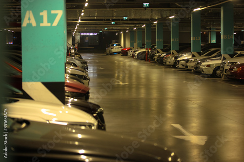Well-lit parking with easy navigation in the mall with many cars in the evening, gray concrete road for traffic and separating numbered poles  © vita