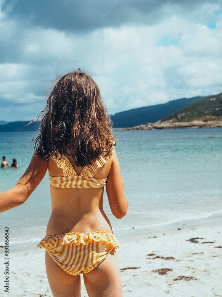 Vertical shot of a back view of little girl in a bikini on the beach with  the sea in the background Stock Photo | Adobe Stock