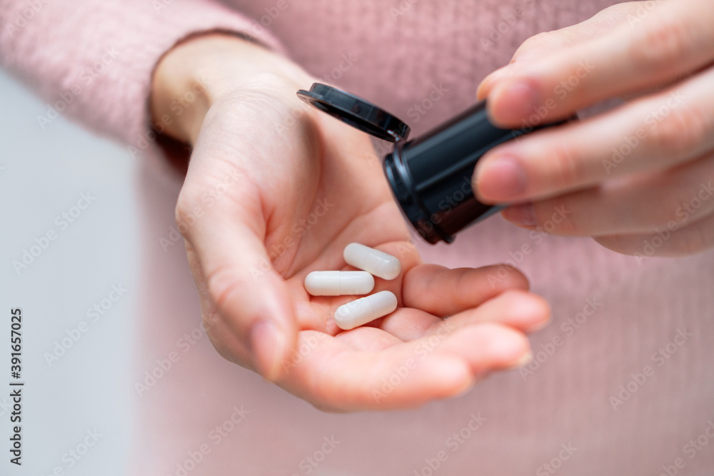 Closeup shot of an unrecognizable woman holding a medication in his hands. Healthcare and medical concept. Female holding three white pills in hand at his home or office. Focus on the pill. Closeup shot of an unrecognizable woman holding a medication in his hands. Healthcare and medical concept. Female holding three white pills in hand at his home or office. Focus on the pill.