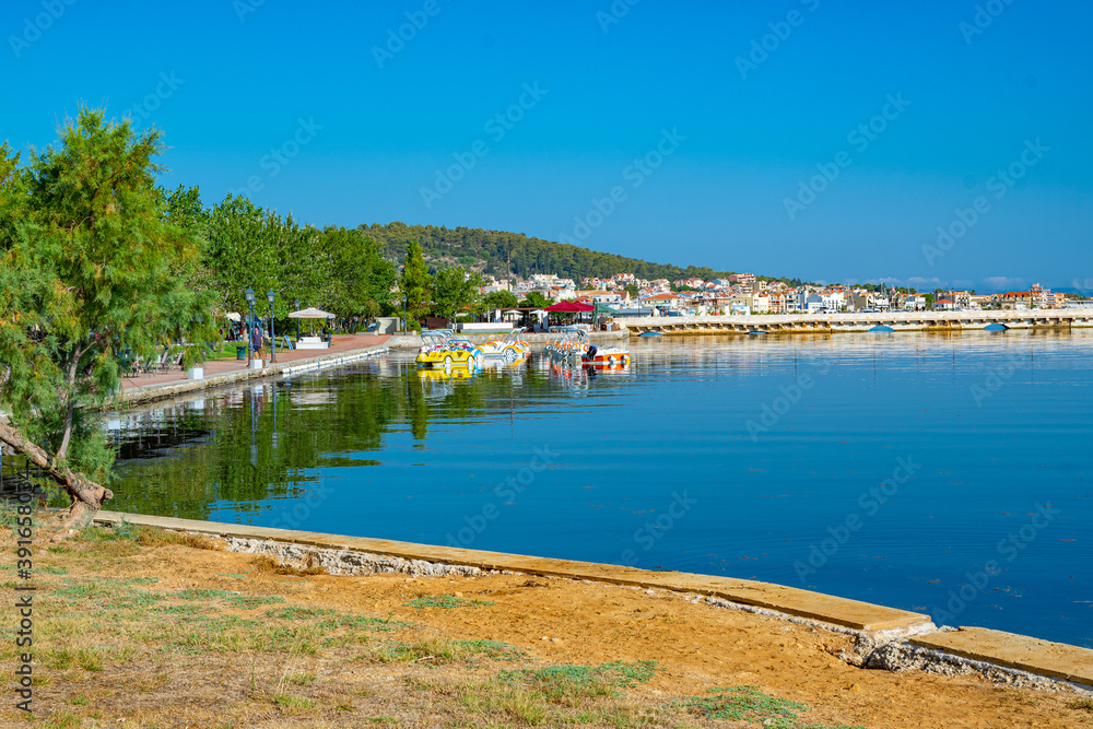 Fototapeta premium Argostoli's tranquil Koutavos Lagoon reflects a vibrant scene of colorful boats and a picturesque waterfront.The iconic De Bosset bridge stretches across the calm waters, connecting the town