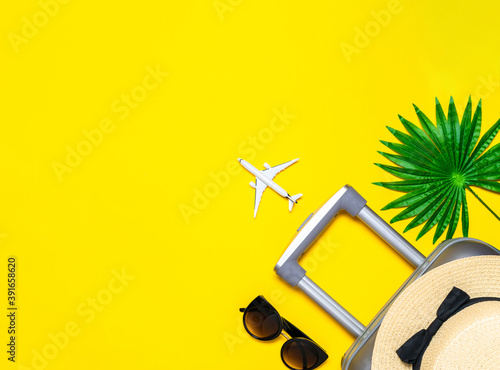 Summer background table. Suitcase, sunglasses with palm leaves and straw hat, white plane in travel composition on yellow background. Copy space, summer vacation and business travel concept.