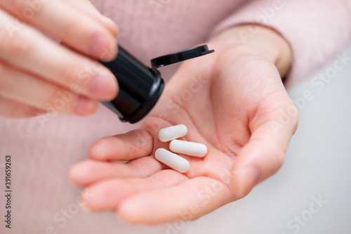 Closeup shot of an unrecognizable woman holding a medication in his hands. Healthcare and medical concept. Female holding three white pills in hand at his home or office. Focus on the pill.