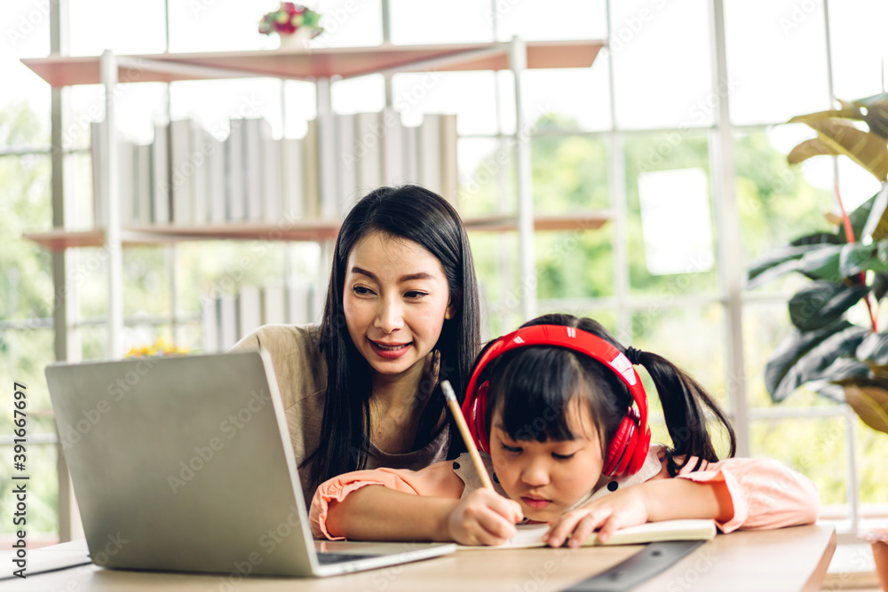 Mother and asian kid little girl learning and looking at laptop computer making homework studying knowledge with online education e-learning system.children video conference with teacher tutor at home Mother and asian kid little girl learning and looking at laptop computer making homework studying knowledge with online education e-learning system.children video conference with teacher tutor at home
