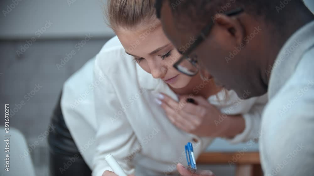 Woman writing something in black man's notebook on english lesson Woman writing something in black man's notebook on english lesson