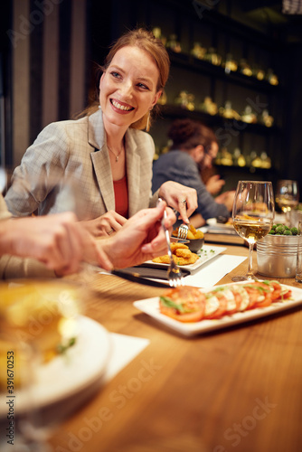 Beautiful smiling caucasian woman sitting in a restaurant with friends and eating dinner.\