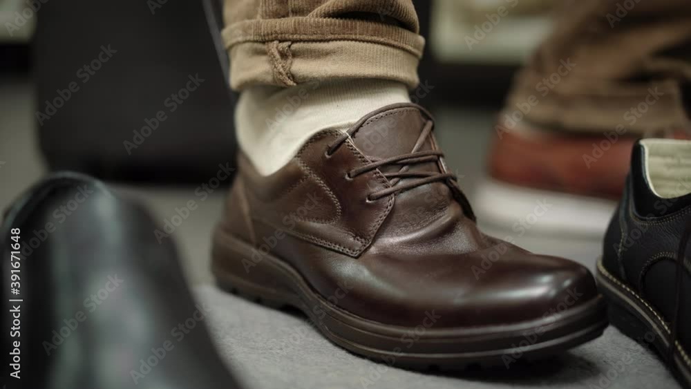 Close-up of male foot with unrecognizable man trying to put on brown boot. Male client trying on too small shoe in store. Shopping and buying. Close-up of male foot with unrecognizable man trying to put on brown boot. Male client trying on too small shoe in store. Shopping and buying.