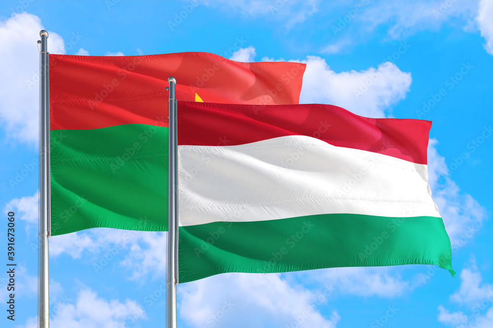 Hungary and Burkina Faso national flag waving in the windy deep blue sky. Diplomacy and international relations concept. Hungary and Burkina Faso national flag waving in the windy deep blue sky. Diplomacy and international relations concept.