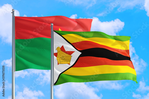 Zimbabwe and Burkina Faso national flag waving in the windy deep blue sky. Diplomacy and international relations concept.